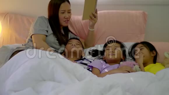 年轻的母亲和她的女儿女孩和儿子在家里的卧室里读一个故事视频的预览图
