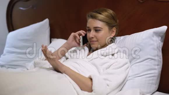 年轻女性躺在床上和朋友打电话看着新修指甲视频的预览图