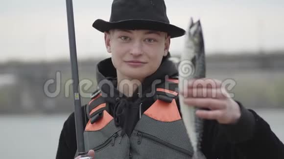 Portait可爱的年轻自信快乐的渔夫一大早就戴着一顶带帽檐的帽子捉扇子展示鱼视频的预览图