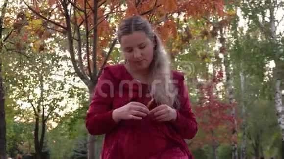 一个年轻的孕妇穿着红色的衣服坐在公园的树下视频的预览图