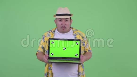 快乐年轻体重超重的亚洲游客一边说话一边拿笔记本电脑视频的预览图