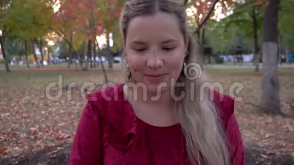 一个年轻的孕妇穿着红色的衣服坐在公园的树下视频的预览图