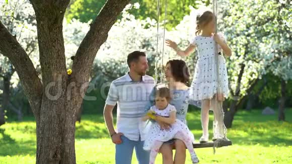 幸福的家庭男人亲吻女人她们的女孩在春天的花园里摇摆视频的预览图