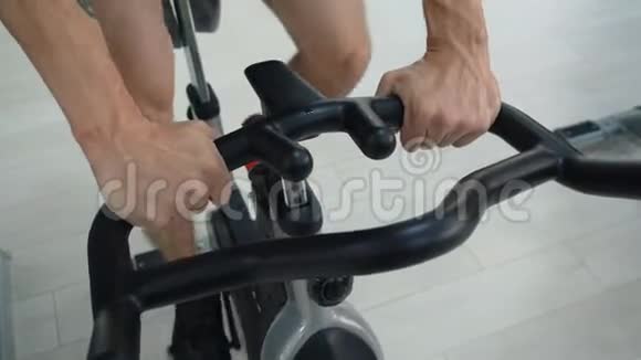 在健身俱乐部男性手拿着手柄静态自行车运动员训练健身房自行车在室内自行车在健身房健身男子视频的预览图