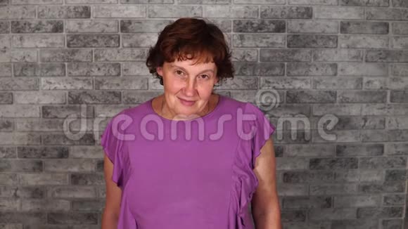 一个漂亮的成熟女人穿着休闲服短发微笑着在灰色的砖块背景上看着相机视频的预览图