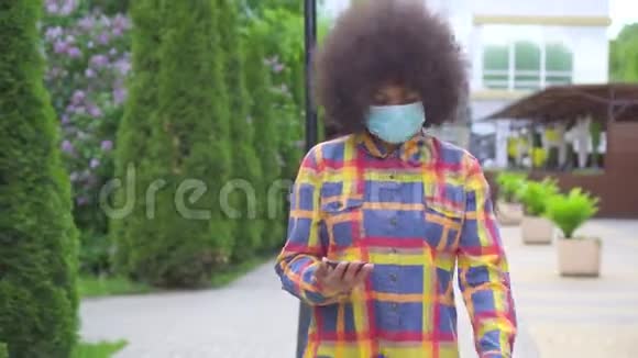 美国黑人妇女肖像留着非洲发型戴着一个带智能手机的保护性医疗面具视频的预览图