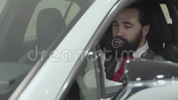坐在新车客厢里的成功大胡子男士在新车的内部检查视频的预览图