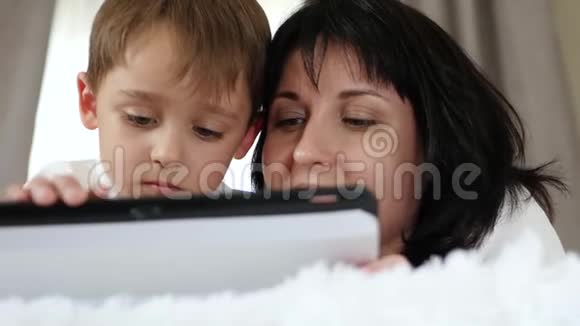 一个女人和一个孩子的肖像一个母亲和一个小男孩用平板电脑打电话看电影并访问视频的预览图