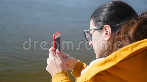一个女孩在智能手机上拍摄一条河特写镜头晴天秋天的天气视频的预览图