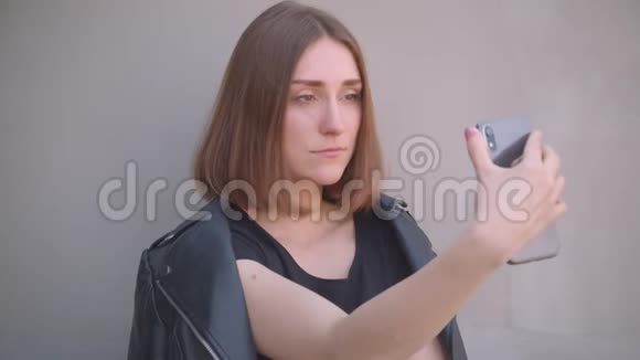 年轻漂亮的白种人女孩穿着皮夹克在城市户外打电话自拍的特写照片视频的预览图