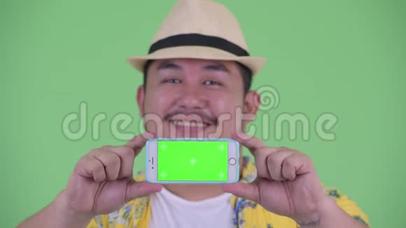 一位年轻体重超重的快乐亚洲游客一边看电话一边思考视频的预览图