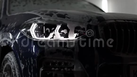 蓝色高级SUV上洗车前照灯特写泡沫顺着汽车流下视频的预览图