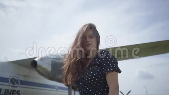 快乐的年轻黑发女孩微笑着看着镜头前的大白飞机头发随风飘扬视频的预览图