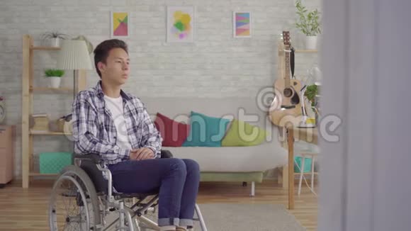 悲伤的亚洲年轻人坐轮椅在客厅里视频的预览图