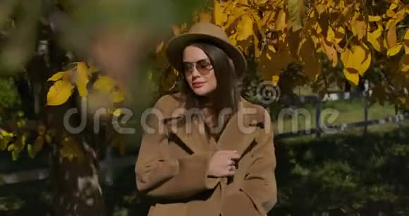 自信的欧洲女孩戴着棕色帽子和太阳镜在秋天公园的镜头前摆姿势优雅的白人年轻女子视频的预览图