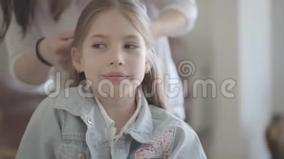 美丽的女孩一头浅长发坐在椅子上妈妈为一个可爱的孩子做发型视频的预览图