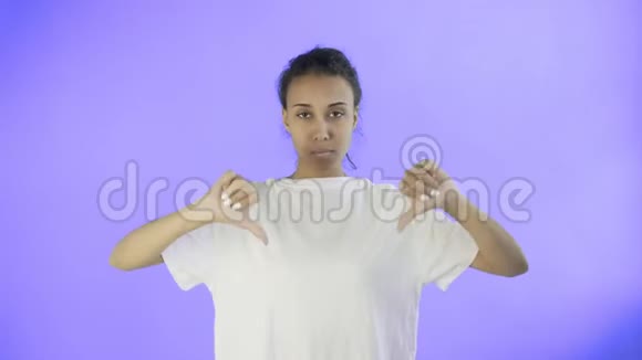 穿着白色t恤的漂亮少女拇指朝下双手放在紫色背景上视频的预览图