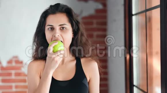 西班牙裔微笑健身少女吃新鲜绿苹果看镜头的肖像视频的预览图