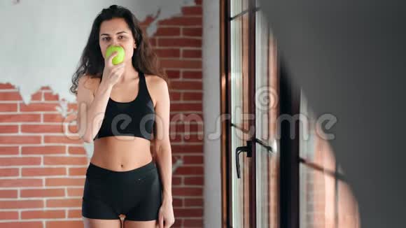 可爱的年轻健身女士微笑着在阁楼的背景下吃美味的苹果视频的预览图