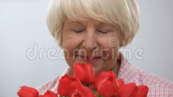 可爱的老太太闻着郁金香的花束享受着香气对着镜头微笑视频的预览图