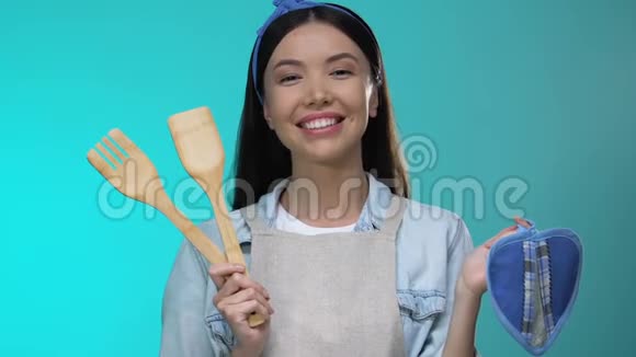 积极的家庭主妇拿着厨具对着镜头微笑上烹饪课视频的预览图