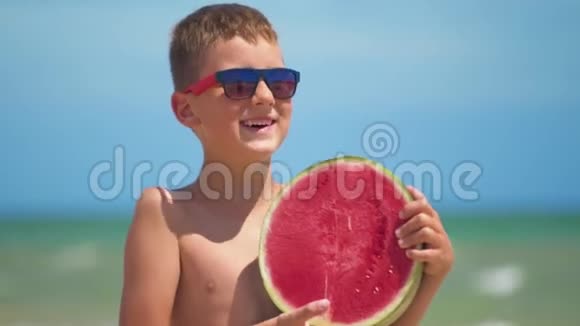 戴眼镜的男孩在大海的背景上抱着一个明亮的西瓜视频的预览图