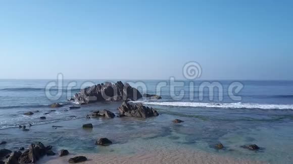 蓝色的海水环绕着沙质海岸线上的褐色岩石视频的预览图