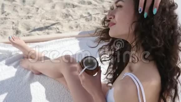 在度假村度夏休息时喝鸡尾酒的女孩美丽的女士在岸挥舞着你好的手手里拿着椰子的女人视频的预览图