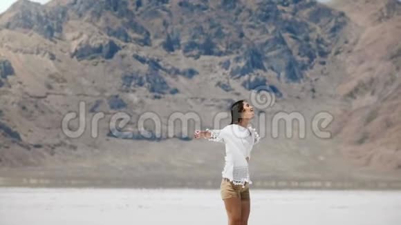 镜头跟随年轻快乐的女人微笑张开双臂闭上眼睛享受在盐漠湖的快乐时刻视频的预览图