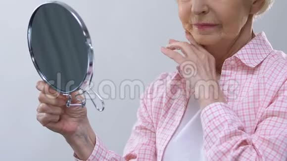 年老的女人照镜子摸着皱纹的脸想着失去的美丽视频的预览图