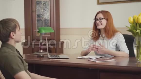 坐在心理医生办公室里的年轻人戴眼镜的漂亮红发年轻女心理学家视频的预览图