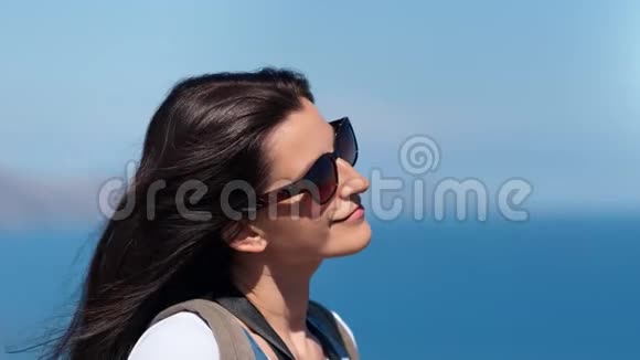 戴墨镜的可爱女旅行者在海空背景下玩头发的特写视频的预览图