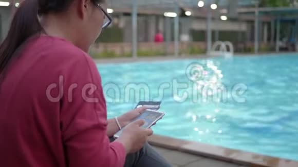 在游泳池附近用信用卡和智能手机在线支付的女人视频的预览图