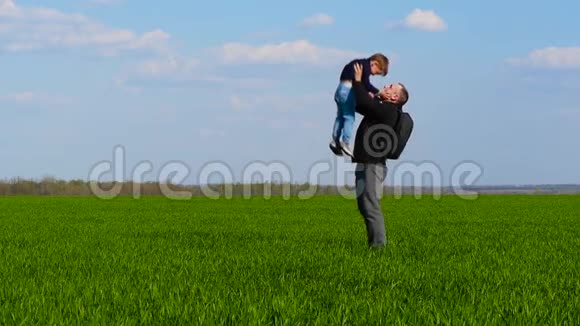 一个快乐的孩子穿过绿草跑到父亲的怀里父亲把孩子抱在怀里把他扔出去视频的预览图