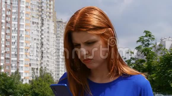 年轻漂亮的红发女孩在城市里在手机里找不到信息视频的预览图