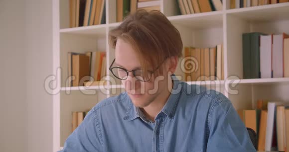 戴眼镜的有魅力的白种人男学生在办公室室内使用平板电脑做笔记的特写照片视频的预览图