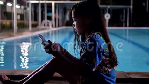 亚洲儿童女孩使用智能手机在游泳池附近放松视频的预览图