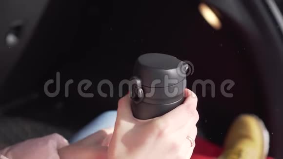 戴着红指甲的女孩坐在车里打开黑色热水瓶的盖子喝茶视频的预览图