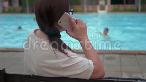 在游泳池附近用手机的女人在等她的女儿视频的预览图