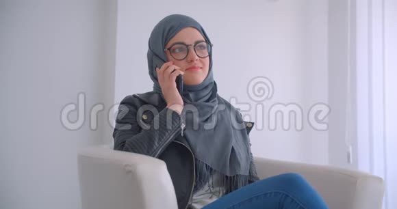 年轻漂亮的穆斯林女商人戴着头巾戴着眼镜坐在电话里说话的特写照片视频的预览图