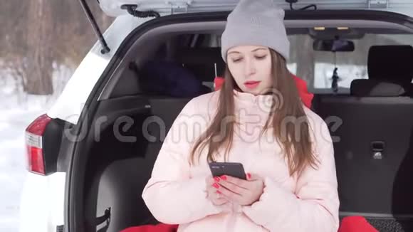 穿着灰色帽子和粉红色夹克的漂亮女孩开着白色的车来到冬季公园视频的预览图