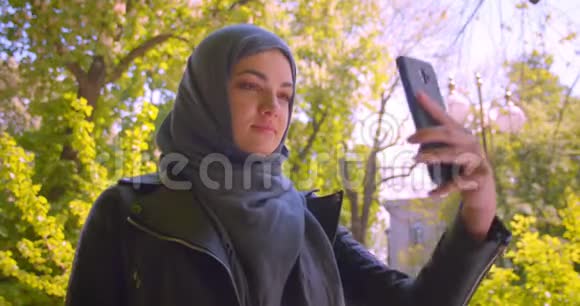 在城市里年轻漂亮的穆斯林女性戴着头巾带着自拍开心地微笑着在电话中拍摄特写镜头视频的预览图