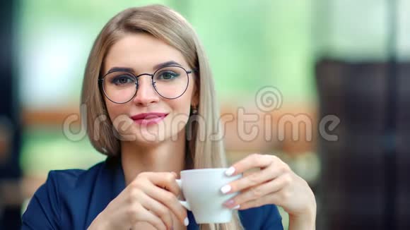 戴着时髦眼镜微笑着从杯子里喝咖啡的美丽的非正式商务女性画像视频的预览图