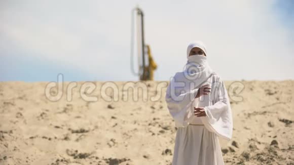 穿着白色衣服的阿拉伯人站在沙漠里背景是石油井架燃料生意视频的预览图