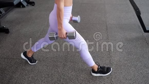性感的女人在健身房里用哑铃做腿上的弓步腿部特写视频的预览图