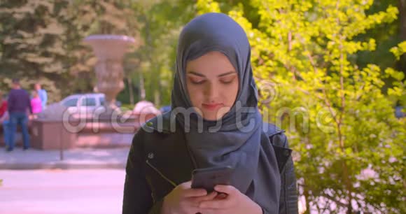 在城市里年轻漂亮的穆斯林女性戴着头巾用手机看着镜头开心地笑着视频的预览图