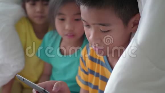 孩子们哥哥和姐姐在床上的毯子下面用平板电脑视频的预览图
