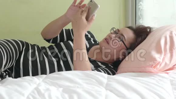 女人用智能手机躺在卧室的床上在网瘾中聊天和发送信息视频的预览图