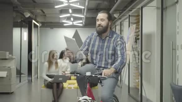 长胡子的微笑男子骑着自行车手里拿着文件向办公室里的女士展示文件很漂亮的女人视频的预览图
