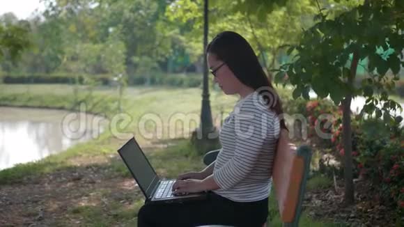 女人拿着笔记本电脑坐在户外公园里视频的预览图
